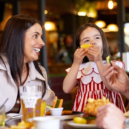 A child seated at an indoor table with parents, enjoying food.