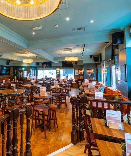The bar and interior restaurant seating area of the Blue Posts in St James's, with upholstered booth seats, TVs on the walls, and glasses hanging in racks above the bar.