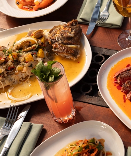 An advertising image of a selection of dishes and various drinks sat on a table within the interior restaurant and seating area at The Ubiquitous Chip.