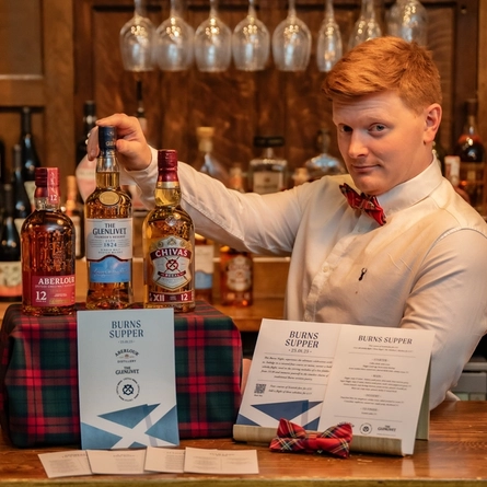 An image of a member of staff stood behind the bar next to a display of 3 bottles of Whiskey within the interior function room during a Burns Night Event at The Crabtree.