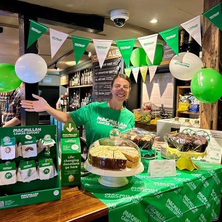 An image of various cakes and pin badges set up on an interior bar to raise money for Macmillan at a Greene King venue.