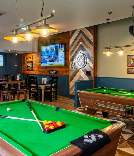 The interior pub games area with two pool tables, a dart board and TV's on the wall with the seating area in the background at the Armstrongs.