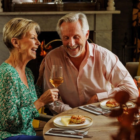 An image of 2 people enjoying Cheese Night dishes and white wine within the interior restaurant and seating area at The Foundry Bell.