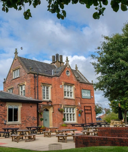 An image of the exterior facade and beer garden seating area at The Guild.