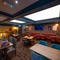 An upper floor interior restaurant seating area at the Old School House, with a long, upholstered booth seat along one side of the room, framed artwork and a TV on the wall above it, and large, square sky lights in the ceiling.