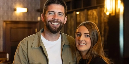 A close up of two people standing inside of a pub.