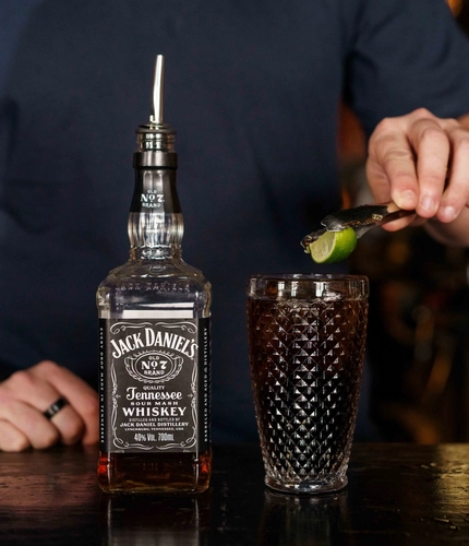 A lime wedge being dropped into a glass of Jack Daniels & Coca-Cola.