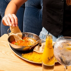 A hand dipping a poppadom into a balti dish containing curry on an indoor table.
