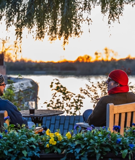 An image of 3 friends with drinks sat at a table within the exterior beer garden seating area with waterside view at The Crabtree.