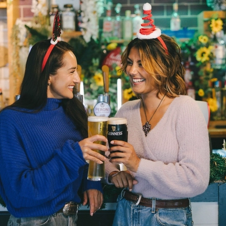 An image of 2 friends enjoying drinks stood at the interior bar within a Greene King venue.