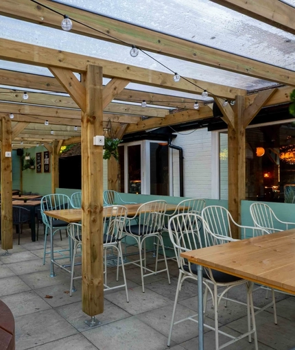 The undercover exterior beer garden seating area at The White Hart in Frimley, with a TV on the wall.