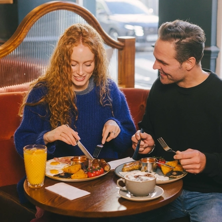 A lifestyle image of 2 friends enjoying breakfast dishes and drinks within the interior restaurant seating area at an Urban Core Venue.