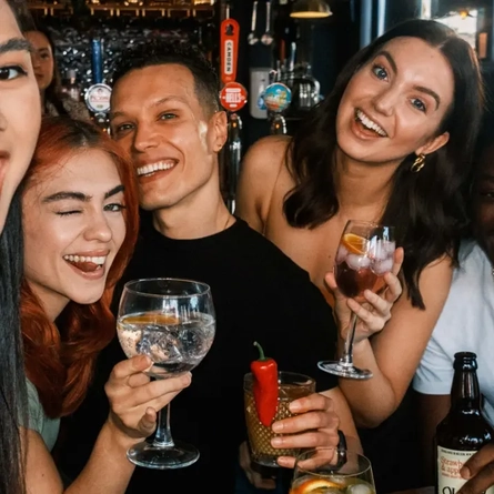 A group of people posing for a selfie with drinks in their hands.