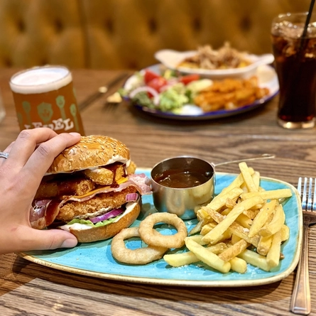 Plated dishes for Burger of the Month October served at Greene King Pubs.  A hand is holding a burger.