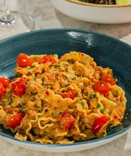 An advertising image showing a bowled Crab Mafalde Pasta dish sat on a table within the exterior beer garden seating area at a Crafted venue.