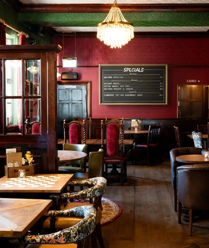 The interior restaurant seating area at the King's Head in Bayswater, with dark wood floors, upholstered chairs, and a fireplace.