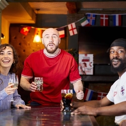 A mixed group of people, sitting at an indoor table reacting to sport event.
