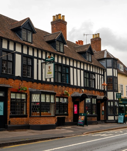 A view from across the road of the exterior facade and signage of The Talbot in Worcester; with flower baskets hanging from the brick walls.