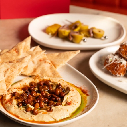 An advertising image of 3 snack dishes and drinks sat on a table within the interior restaurant and seating area at The Ubiquitous Chip.