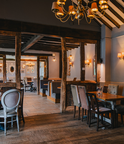 The interior restaurant seating area of The Green Man, with upholstered booth seating, framed artwork and mirrors on the wall, and wooden beams.
