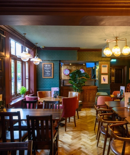 The upper floor interior restaurant seating area at The Globe in Marylebone; with parquet flooring, wood panelled walls, interactive darts, and a TV on the wall.