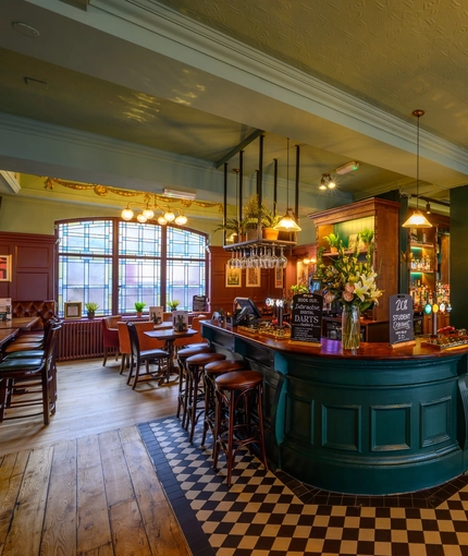 The bar and interior restaurant seating area at The Globe in Marylebone; with checkerboard tiles in front of the counter, TVs on the walls, and bar stool seating.
