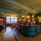 The bar and interior restaurant seating area at The Globe in Marylebone; with checkerboard tiles in front of the counter, TVs on the walls, and bar stool seating.