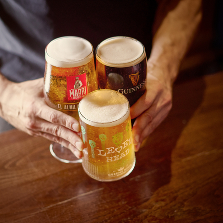A lifestyle image of a customer placing 3 drinks down on a wooden table within the interior seating area at a Chef & Brewer venue.