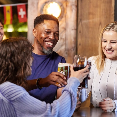 A mixed group of people inside a pub, smiling and clinking glasses in a Cheers motion.