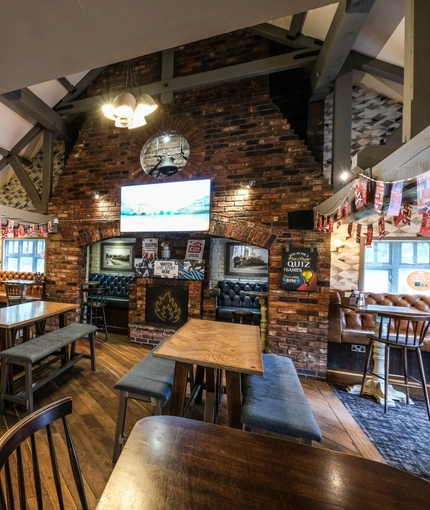 Interior dining area of a pub with a fireplace, a gambling machine and a TV.