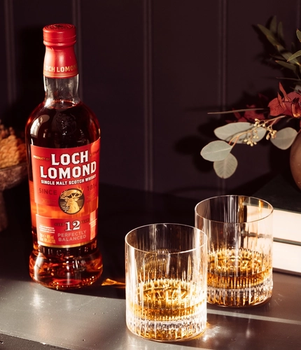 A full bottle and two glasses of Loch Lomond whisky sitting on a table.