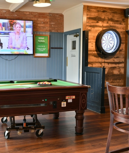 Interior seating area of a pub with a pool table, a dartboard and a TV.