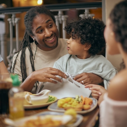 A family of four sitting at a table laden with plates of food and drinks.