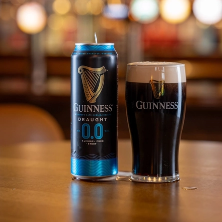 A Guinness can next to a pint of beer on a wooden table of a pub