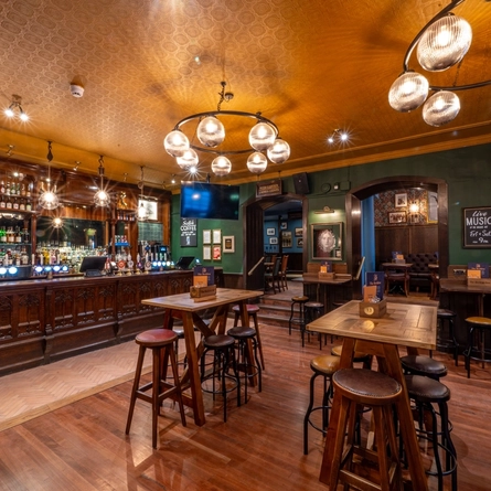 The bar and interior restaurant seating area at The Beehive Inn, with a TV hanging from the ceiling, bar stool seating, and gothic window style carvings on the front of the bar.