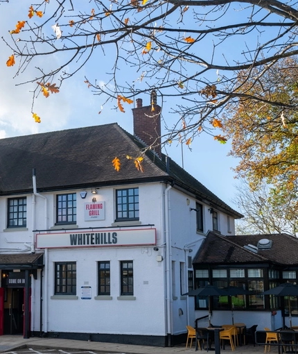 The exterior facade, signage, and beer garden seating area of Whitehills in Northampton, with shade umbrellas over some of the tables.