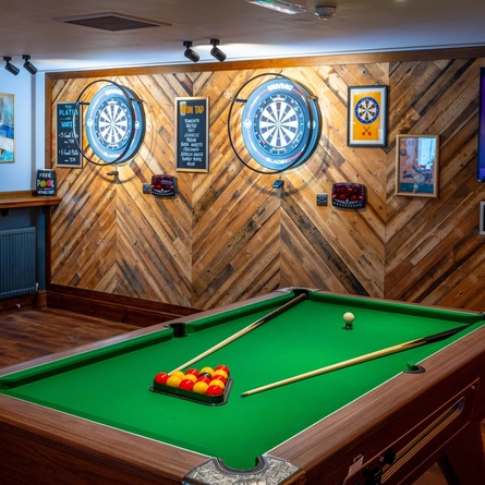 The interior games area at the Counting House, with two dartboards, a TV on the wall, and a pool table.