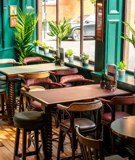 A close up view of the restaurant tables next to the windows inside the Phoenix in Bayswater; with padded seats and bar stools, and potted plants on the window sills.