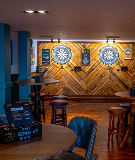 The interior games area at the Counting House, with TVs on the walls, two illuminated dartboards, a pool table, and restaurant seating nearby.