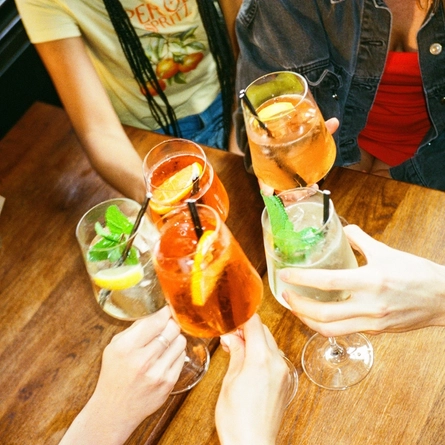 A image focused on a group of drinks being held in a 'cheers' position around a table in a Greene King venue in London.