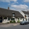 A view from across the road of the exterior facade and signage of The Royal Oak in Bishops Cleeve, with a thatched roof, and flower baskets hanging on the walls.