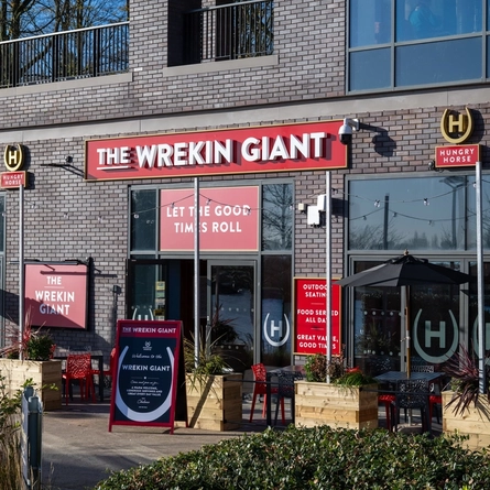 The exterior facade, signage, and beer garden seating area at The Wrekin Giant in Telford, with shade umbrellas on some of the tables, and string lights over the seating area.