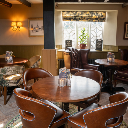 An interior restaurant seating area at The Blue Cap, with patterned brick flooring, wooden beams on the ceiling, and large, upholstered chairs.