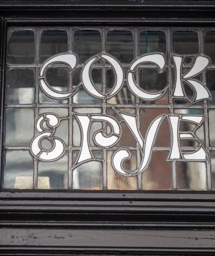 A close up view of a stained glass sign inlaid with the words "Cock & Pye".