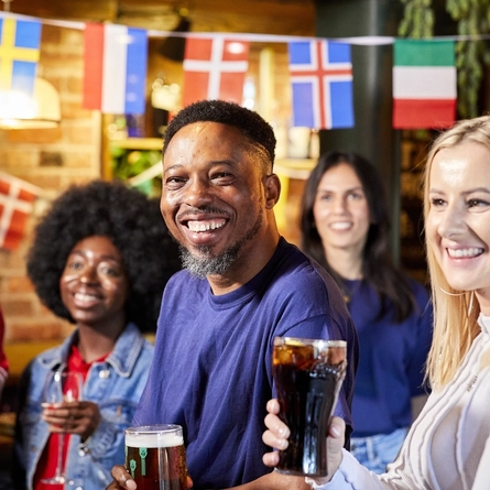 A mixed group of people holding drinks and watching a sporting event.