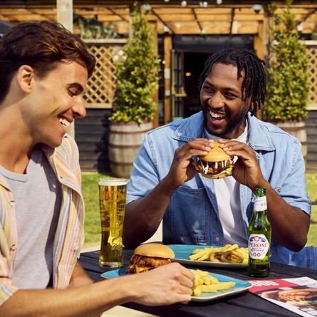 A group of friends all sat round a table with meals and drinks served in the exterior beer garden at a Flaming Grill venue.