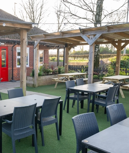 The exterior beer garden seating area at The Weathervane in Stoke On Trent, with sheltered areas and string lights above the tables.