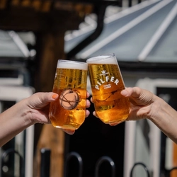 A close up lifestyle image showing 2 people holding pints of Pilfer Peach Lager and celebrating with a cheers.