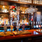 A close up view of the beer taps and golden drinks trays on the bar inside the Two Chairmen in St James's, with glass tankards hanging above the counter, and bottles of wine and alcoholic spirits on shelves behind the bar.