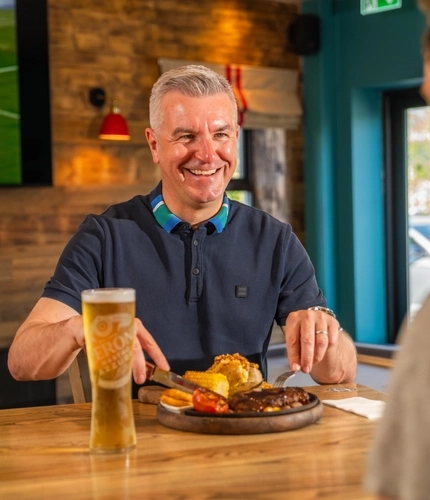 A close up of a father sat in the interior restaurant and seating are eating a main meal of steak smiling on Fathers day at a Flaming Grill venue.